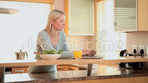 女人在喝橙汁之前在笔记本电脑上打字视频的预览图