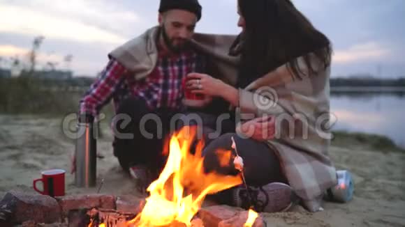 一对恋爱中的情侣坐在湖边的篝火旁聊着天喝着热茶视频的预览图