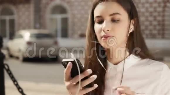 年轻时尚漂亮的女孩与电话摆在城市街道青少年模型有耳机视频的预览图