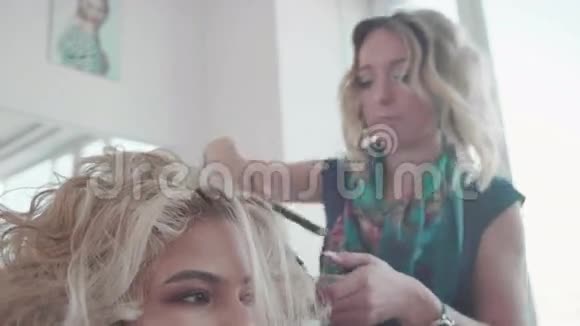 女理发师用卷发熨斗在金发上做卷发视频的预览图
