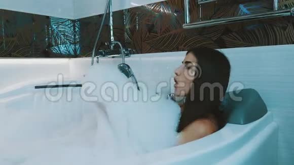 快乐的女孩在浴室里洗了满是泡沫的澡浴缸吹肥皂泡沫视频的预览图