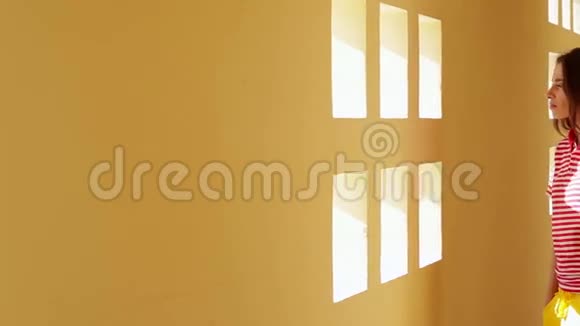 美丽的黑发年轻女子站在靠近白色墙壁和小窗户视频的预览图