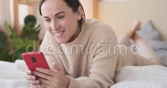 快乐的女人在床上用手机视频的预览图