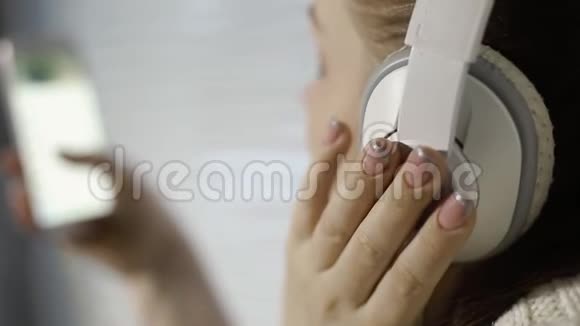 休息和放松年轻的高加索女人坐在窗台上用智能手机用耳机听音乐视频的预览图