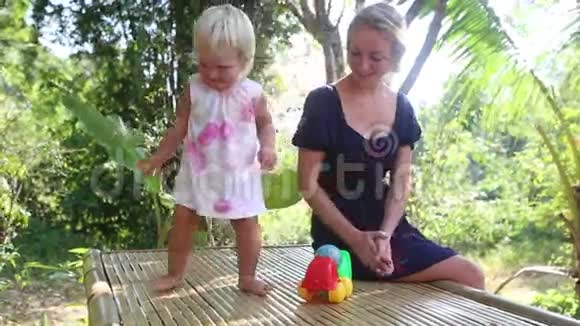 日出时一个金发小女孩在热带树下和母亲跳舞视频的预览图