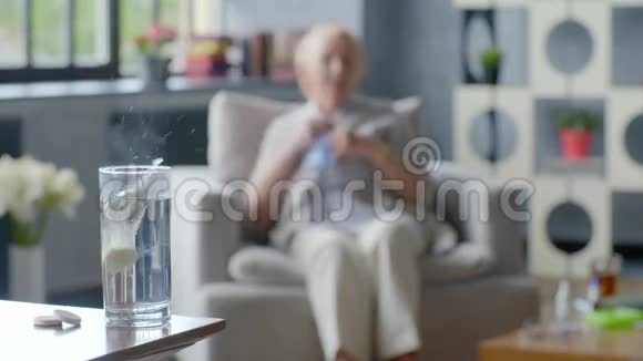 生病的老年妇女咳嗽在杯中服药的背景下抱着头视频的预览图