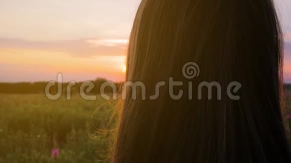 田野里年轻漂亮的女孩看着夕阳近距离射击五彩缤纷慢动作视频的预览图