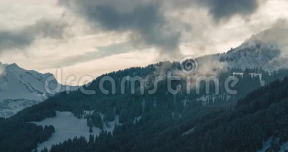 在奥地利阿尔卑斯山的日落中从雪林中升起的云层的时间流逝视频的预览图