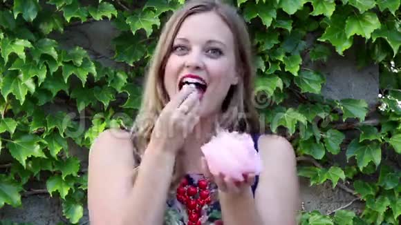 年轻女子笑着吃着带常春藤背景的粉红棉花糖视频的预览图
