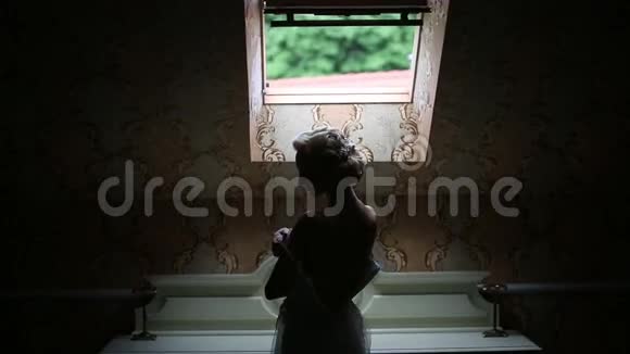 优雅的白种人新娘穿着婚纱站在窗前视频的预览图
