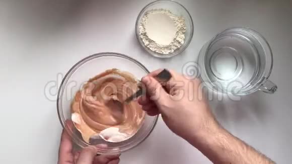 一个男人正在做古拉什酱用勺子将番茄酱酸奶油和面粉放入玻璃容器中搅拌加水再混合视频的预览图