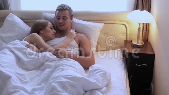 一对年轻漂亮可爱的夫妇早上躺在床上拥抱和微笑视频的预览图