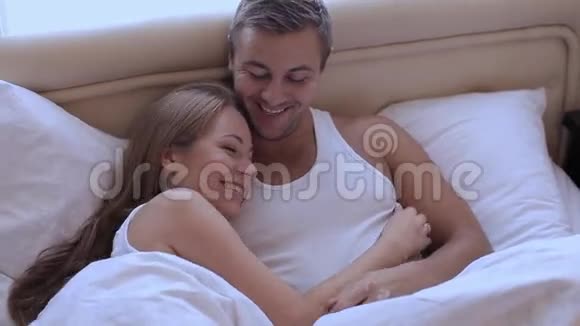 一对年轻漂亮可爱的夫妇早上躺在床上拥抱和微笑视频的预览图