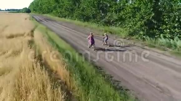 穿裙子的女孩和一个孩子骑着自行车沿着麦田用无人机射击从美丽的风景视频的预览图