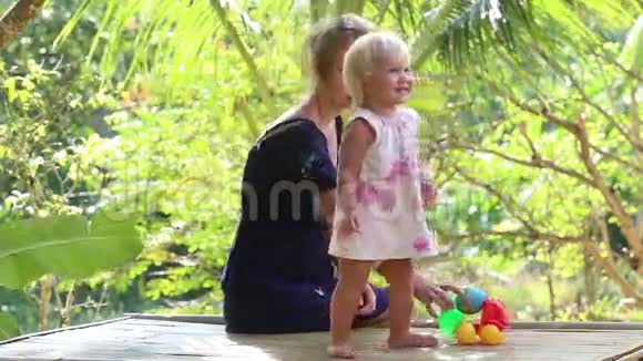 日出时一个金发小女孩在热带树下和母亲跳舞视频的预览图