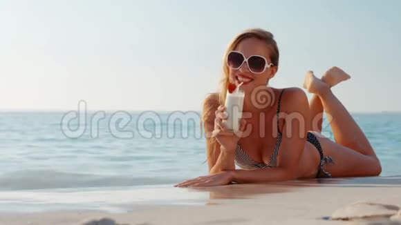 快乐的金发美女躺在沙滩上喝鸡尾酒视频的预览图