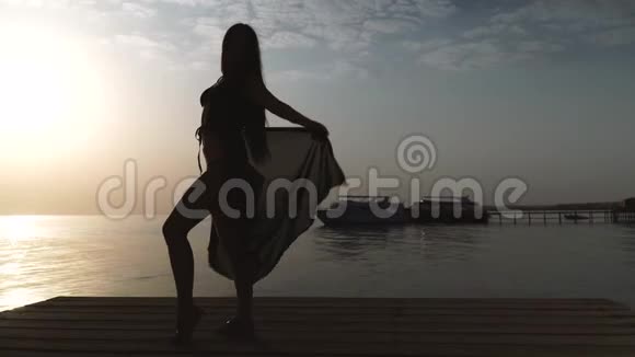 一个穿着泳衣和斗篷的女孩站在码头上迎接黎明视频的预览图