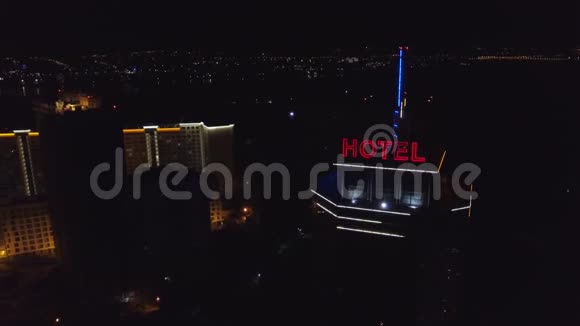 艾琳霓虹灯红色铭文酒店在夜间城市的一座现代建筑的屋顶上旁边是交通车视频的预览图