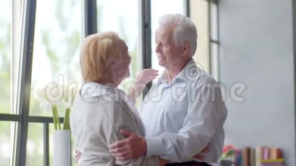 爱和快乐的老年夫妇拥抱和交谈在现代公寓丈夫看着摄像机视频的预览图