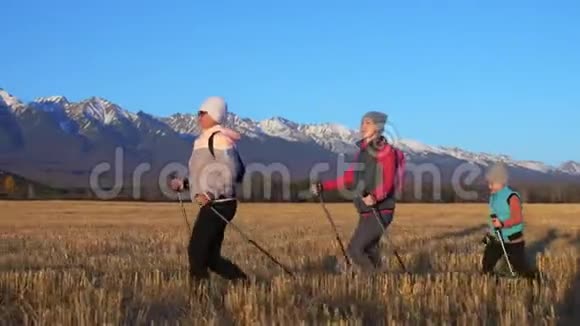 女人在大自然中行走在田野的群山背景下女孩和孩子使用跋涉棒和北欧视频的预览图