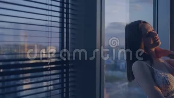 穿着白色内衣的布鲁内特站在窗户旁边视频的预览图