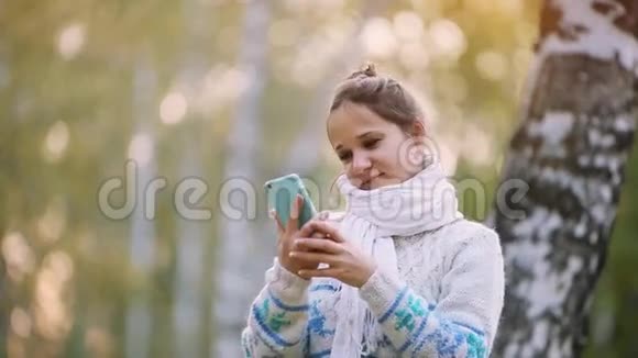 秋天穿着针织毛衣和围巾的微笑女人在公园里用手机自拍1920x1080视频的预览图