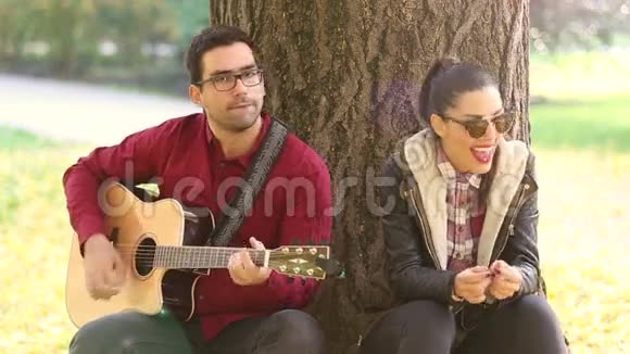 女人笑着男人弹吉他坐在公园的树上视频的预览图