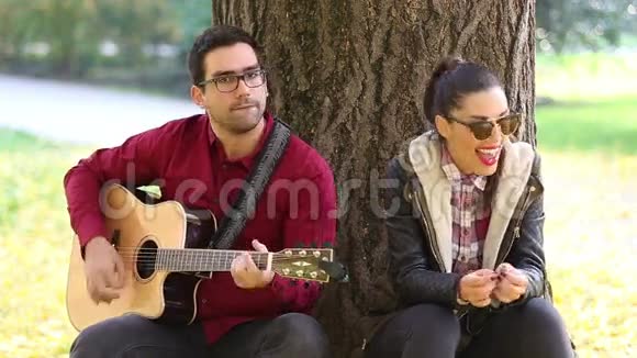 女人笑着男人弹吉他坐在公园的树上视频的预览图