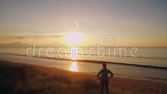 在日落时分一位身材匀称的女士站在沙滩沙丘上视频的预览图