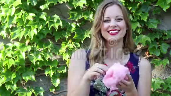 年轻女子微笑着吃着带常春藤背景的粉红棉花糖视频的预览图