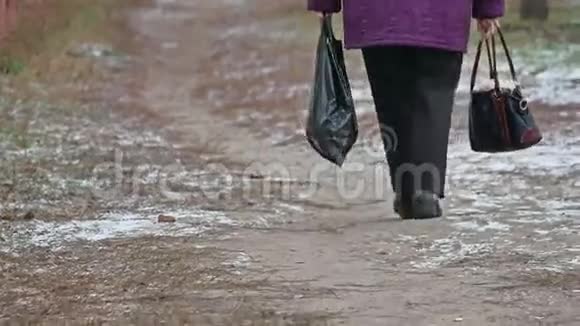 老妇人一瘸一拐地走在街上背着一个袋子和一包深秋的户外用品视频的预览图