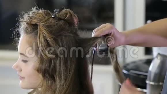 专业的发型师卷起少女的头发视频的预览图