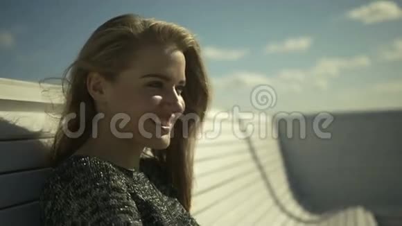 年轻微笑的女人坐在海边某处的长凳上的肖像视频的预览图