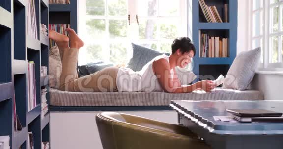 成熟的女人躺在家里的沙发上读书视频的预览图