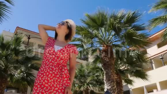 年轻貌美的女人戴着红色的裙子和太阳镜背景是蓝天和棕榈树视频的预览图