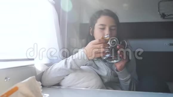 铁路旅行概念窗前的小女孩在车厢里的生活方式火车车厢里喝茶穿深色衣服的女孩喝酒视频的预览图