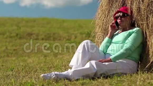 老太太坐在草堆旁用手机交流视频的预览图