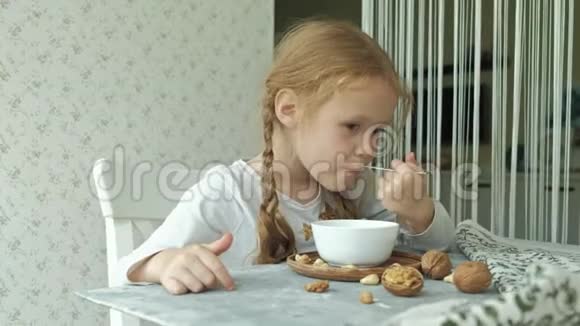 小可爱的女孩早餐吃燕麦片和坚果和干果健康食品概念视频的预览图