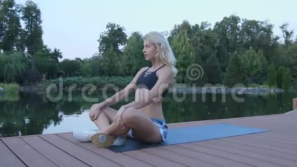 日落时分一个金发的运动女孩正忙着在池塘边伸展视频的预览图