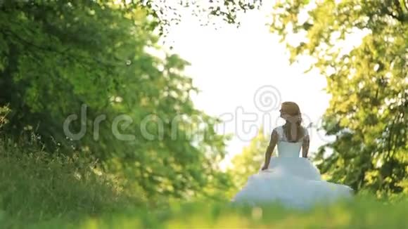 美丽浪漫时尚的金发新娘穿着白色连衣裙在阳光下在森林里跳舞视频的预览图