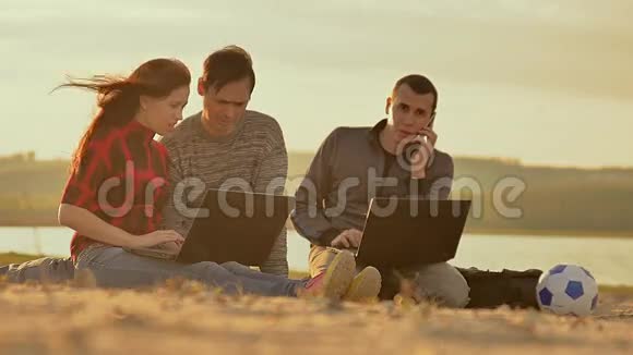在沙滩上用笔记本电脑工作三个人慢动作视频视频的预览图