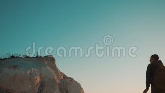 一位男士游客的剪影在日落的生活方式冒险中爬上山顶剪影视频的预览图