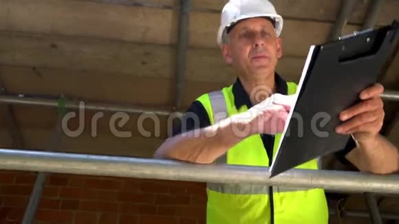男建筑工人工头工人在建筑工地站在脚手架上写在剪贴板上视频的预览图