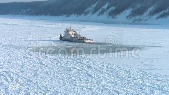 冰封船或拖船在雪林背景下冬季停留在冰雪覆盖的河流上的空中拍摄视频的预览图