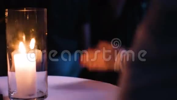 在夜间活动中女性手鼓掌的特写照片坐在桌子旁的女人桌上放着一支燃烧的蜡烛视频的预览图