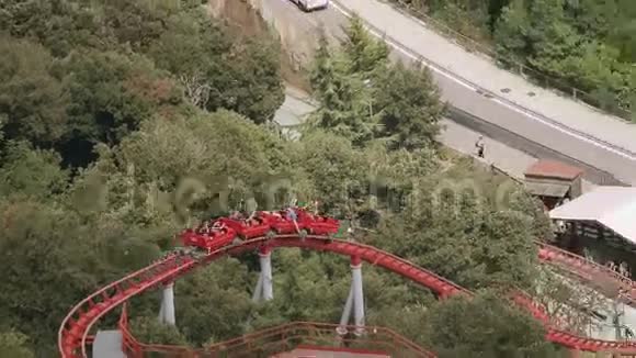 人们在游乐园里坐红色过山车极端快乐夏日绿树树视频的预览图