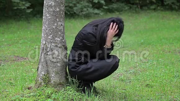 沮丧的女人坐在公园的树旁视频的预览图