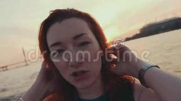 穿着绿松石衣服的年轻女孩在摩托艇上摸头发日落很浪漫微笑视频的预览图