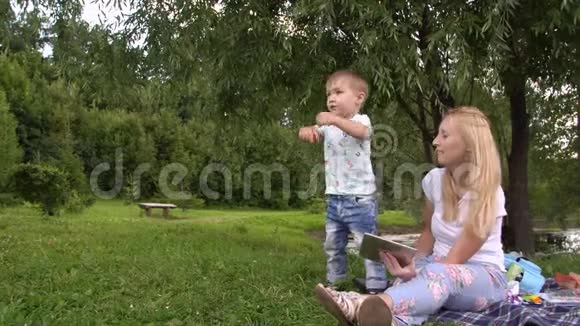 年轻的母亲和小儿子在公园里度过一天妇女和儿童使用平板电脑视频的预览图