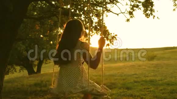 孩子们在公园的秋千上晒太阳年轻女孩在橡木树枝上的绳子上摆动少女喜欢飞行视频的预览图